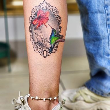 Татуировка колибри с цветком в рамке на ноге