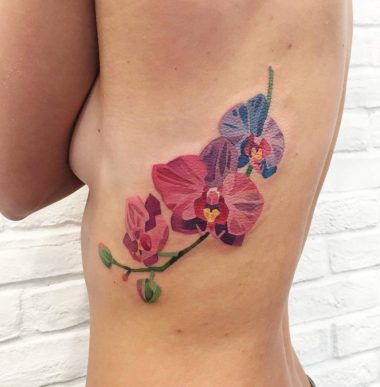 Большая цветная татуировка орхидей на ребрах у девушки